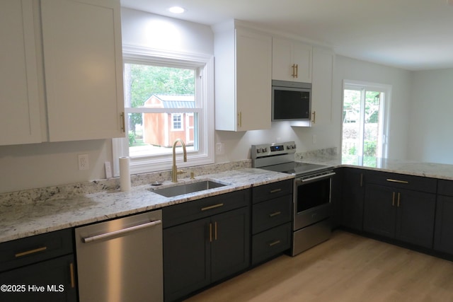 kitchen featuring appliances with stainless steel finishes, a sink, white cabinetry, light wood-style flooring, and light stone countertops