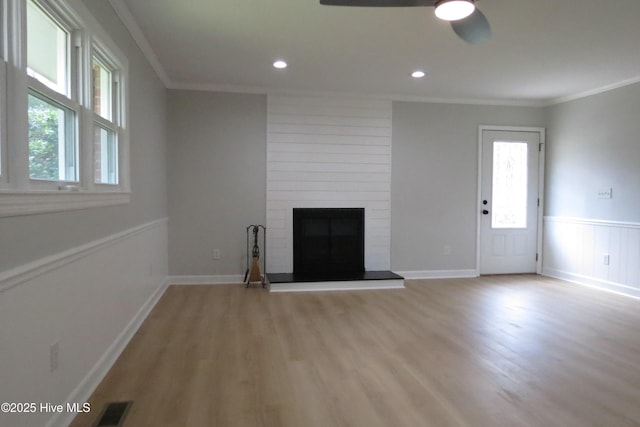 unfurnished living room featuring crown molding, healthy amount of natural light, light wood-style floors, ceiling fan, and a large fireplace