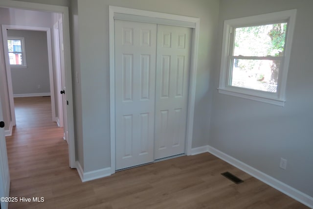 unfurnished bedroom featuring wood finished floors, a closet, baseboards, and multiple windows