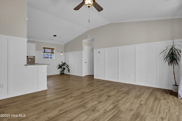 7404 Countywood Way, Wilmington, NC 28411 - unfurnished living room featuring a decorative wall, ceiling fan, lofted ceiling, light wood-style floors, and wainscoting