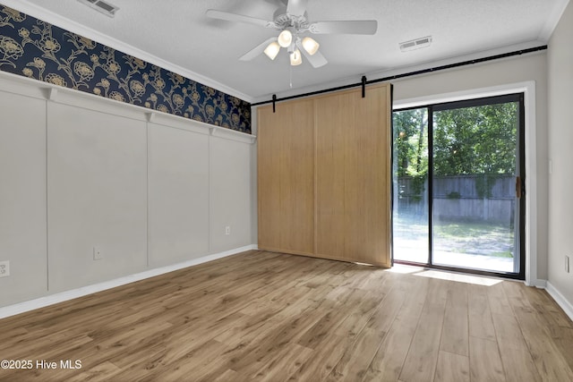 7404 Countywood Way, Wilmington, NC 28411 - empty room with a textured ceiling, wood finished floors, ornamental molding, a ceiling fan, and a barn door