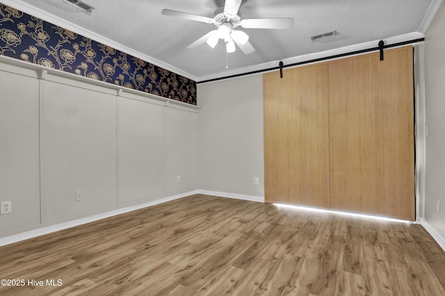7404 Countywood Way, Wilmington, NC 28411 - spare room featuring a barn door, ceiling fan, a textured ceiling, wood finished floors, and ornamental molding