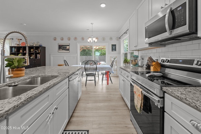 kitchen with appliances with stainless steel finishes, a sink, a chandelier, light wood-style floors, and white cabinets