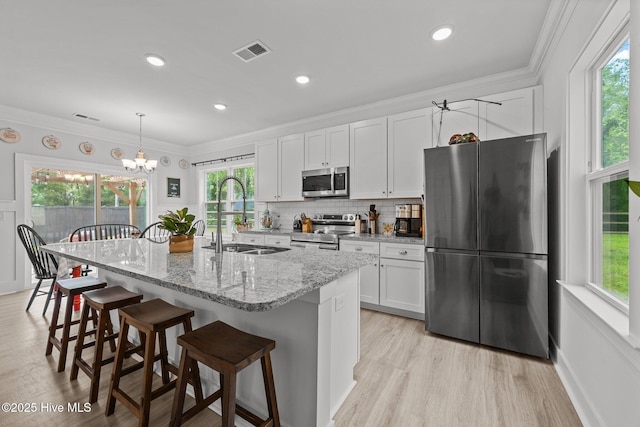 kitchen with stainless steel appliances, a sink, plenty of natural light, white cabinetry, and crown molding
