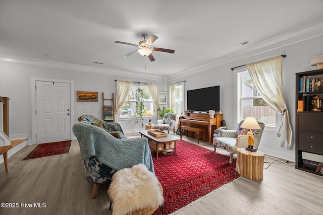 living area with light wood-style floors, crown molding, a ceiling fan, plenty of natural light, and baseboards