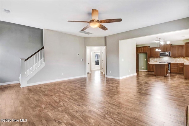 unfurnished living room featuring baseboards, visible vents, ceiling fan with notable chandelier, and wood finished floors