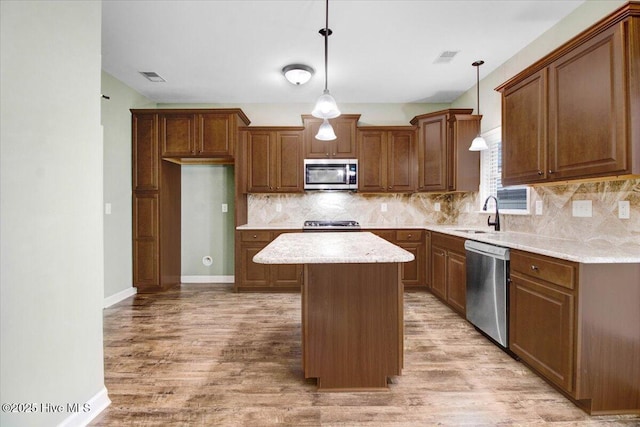 kitchen with decorative backsplash, a sink, appliances with stainless steel finishes, light wood-style floors, and a kitchen island