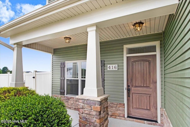 doorway to property with stone siding, a porch, and fence