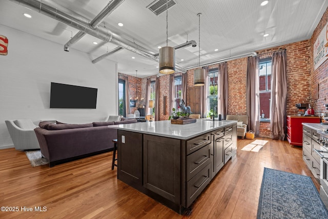 221 Craven St, New Bern, NC 28560 - kitchen with brick wall, light wood-style floors, a center island, a kitchen bar, and dark brown cabinetry