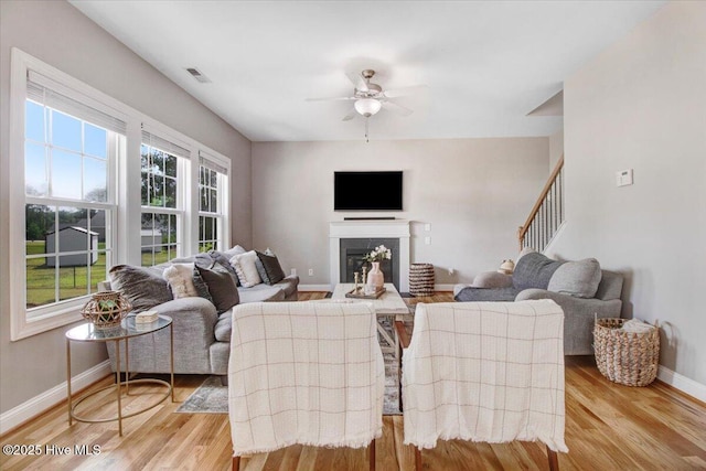 living room featuring a ceiling fan, baseboards, a glass covered fireplace, visible vents, and light wood-type flooring