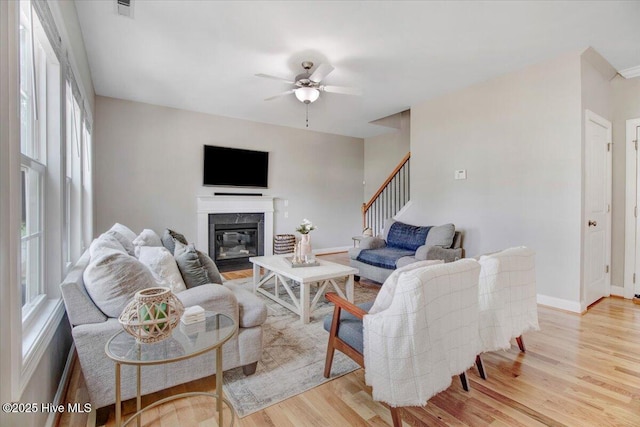 living room featuring visible vents, stairway, a fireplace, light wood-style flooring, and a ceiling fan