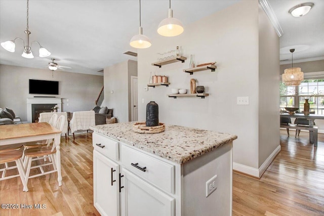 kitchen featuring a ceiling fan, a fireplace, white cabinets, visible vents, and light wood-style floors