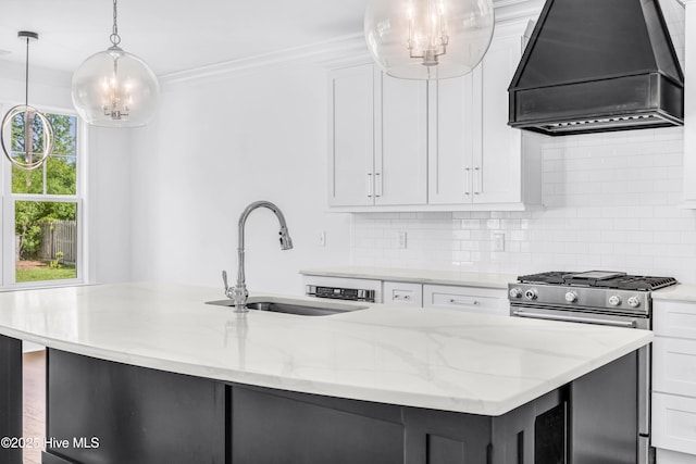 kitchen featuring custom range hood, stainless steel range with gas stovetop, a sink, a chandelier, and an island with sink