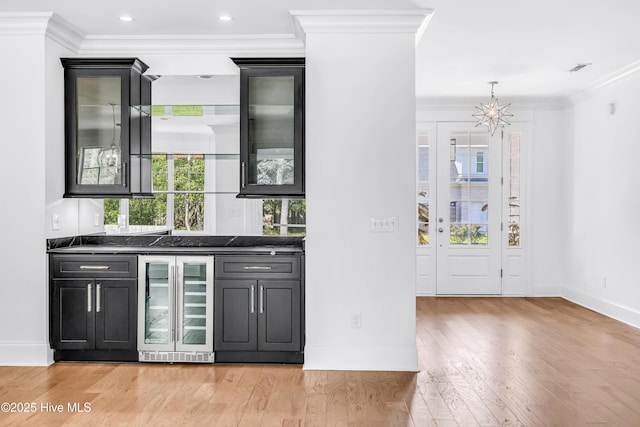 bar with beverage cooler, ornamental molding, baseboards, light wood-type flooring, and a chandelier