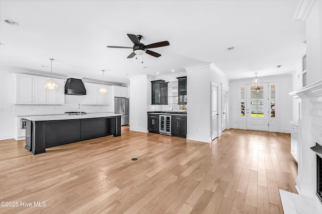 unfurnished living room featuring wine cooler, ornamental molding, ceiling fan, a sink, and light wood finished floors