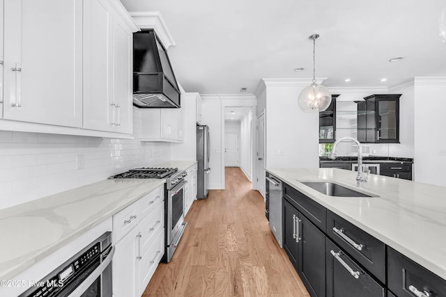 kitchen with stainless steel appliances, custom range hood, a sink, light wood finished floors, and white cabinetry