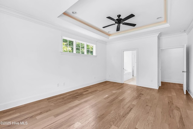 unfurnished bedroom featuring a tray ceiling, ornamental molding, light wood finished floors, ensuite bath, and baseboards