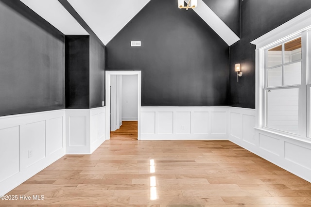 spare room with high vaulted ceiling, a decorative wall, a wainscoted wall, and light wood finished floors