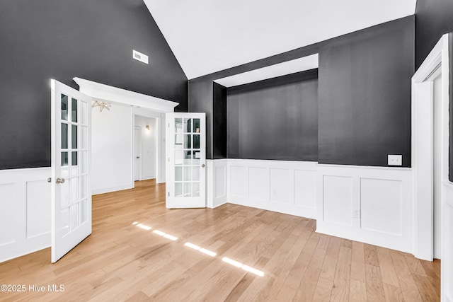 unfurnished living room featuring french doors, a decorative wall, high vaulted ceiling, a wainscoted wall, and wood finished floors