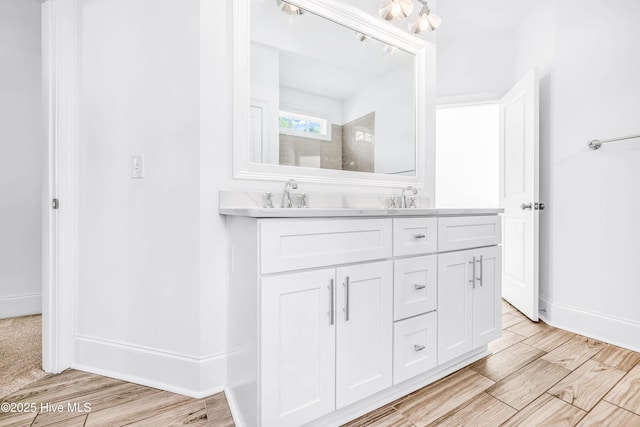 full bath featuring double vanity, tiled shower, baseboards, and wood finished floors