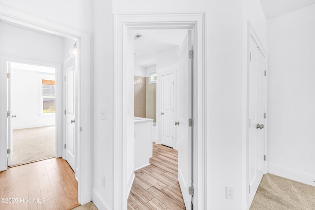 hall with light wood-type flooring, baseboards, and light colored carpet