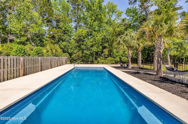 view of swimming pool with a fenced backyard and view of scattered trees