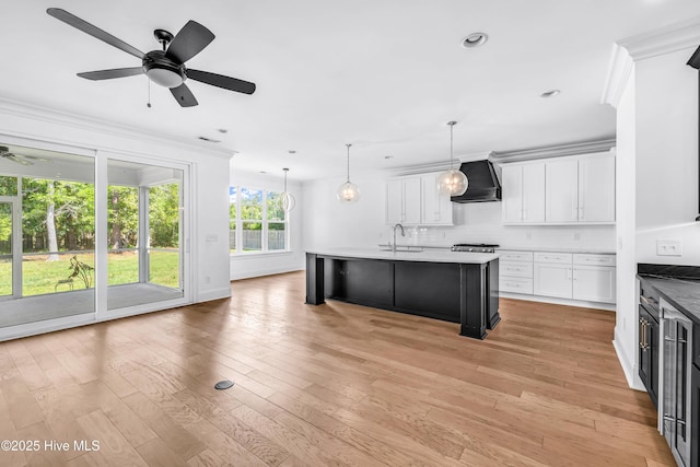 kitchen featuring a sink, wall chimney range hood, ceiling fan, crown molding, and white cabinets