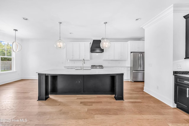 kitchen featuring freestanding refrigerator, custom exhaust hood, a sink, baseboards, and white cabinetry