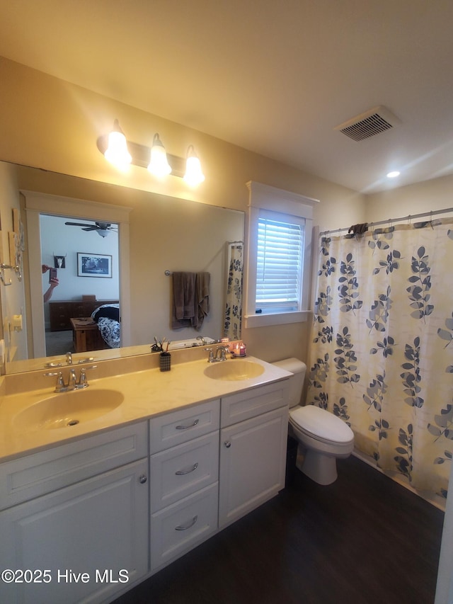 bathroom with ensuite bath, double vanity, toilet, a ceiling fan, and wood finished floors