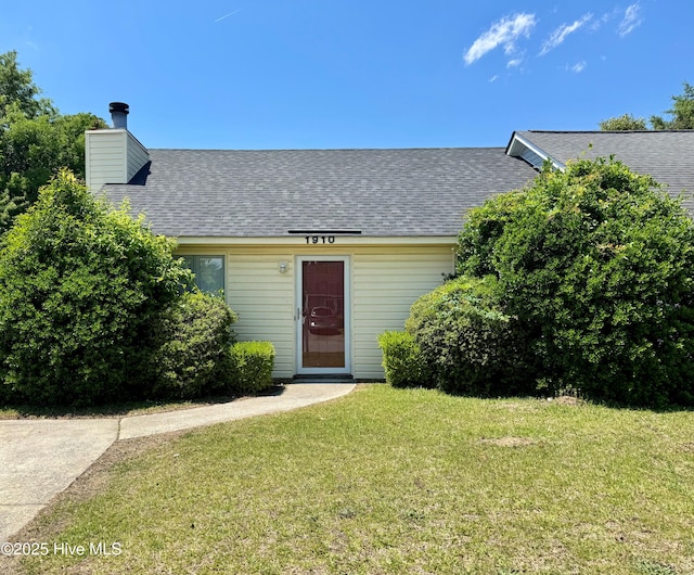 view of front of house featuring a chimney, roof with shingles, and a front lawn