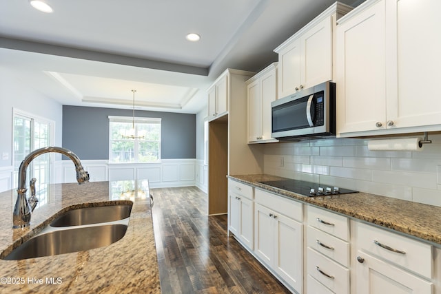 kitchen with stainless steel microwave, a sink, black electric stovetop, dark wood finished floors, and white cabinets