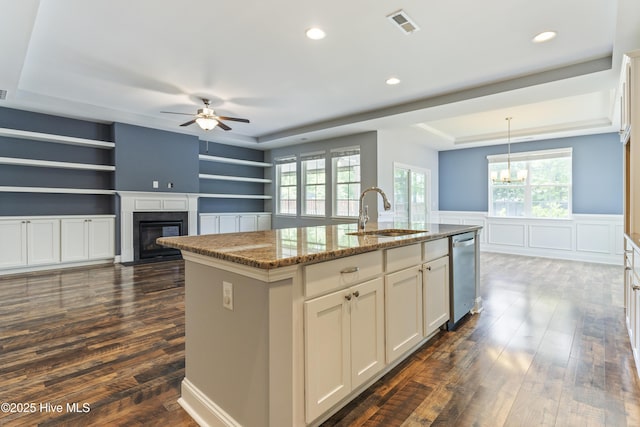 kitchen featuring a sink, stainless steel dishwasher, a ceiling fan, a fireplace with flush hearth, and stone countertops