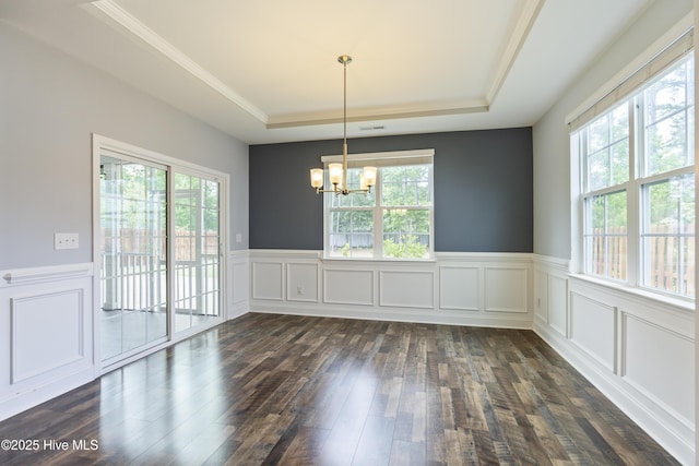 unfurnished dining area featuring a raised ceiling, a chandelier, healthy amount of natural light, dark wood finished floors, and a wainscoted wall