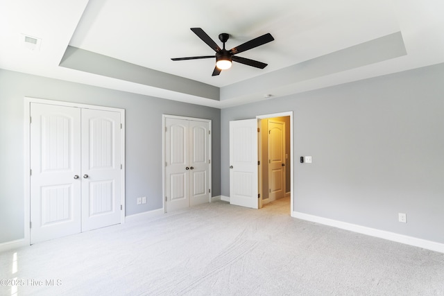 unfurnished bedroom with multiple closets, baseboards, light colored carpet, and a tray ceiling
