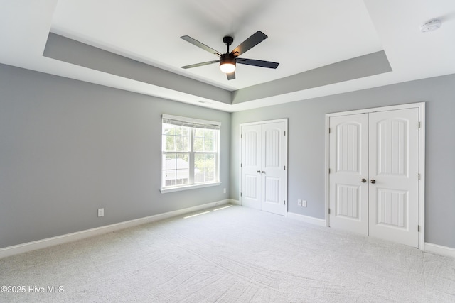 unfurnished bedroom with a tray ceiling, two closets, baseboards, and carpet floors