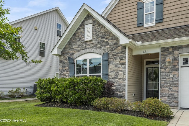 property entrance featuring stone siding, roof with shingles, a garage, and a lawn