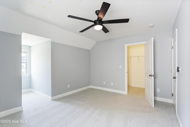 unfurnished bedroom featuring a spacious closet, light colored carpet, vaulted ceiling, baseboards, and a ceiling fan