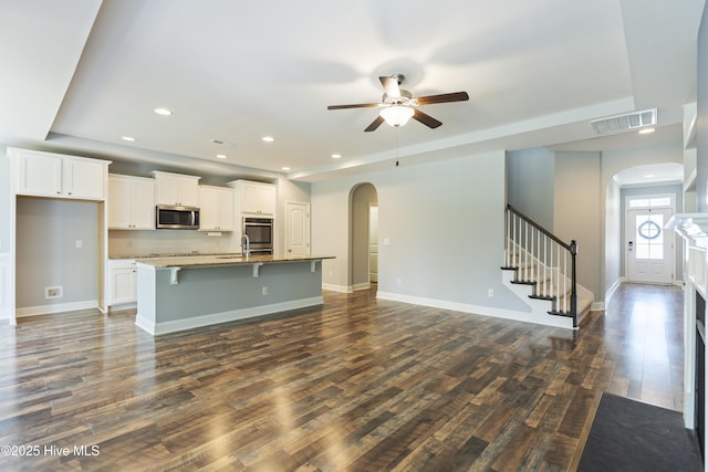 unfurnished living room with arched walkways, dark wood finished floors, a ceiling fan, stairs, and recessed lighting