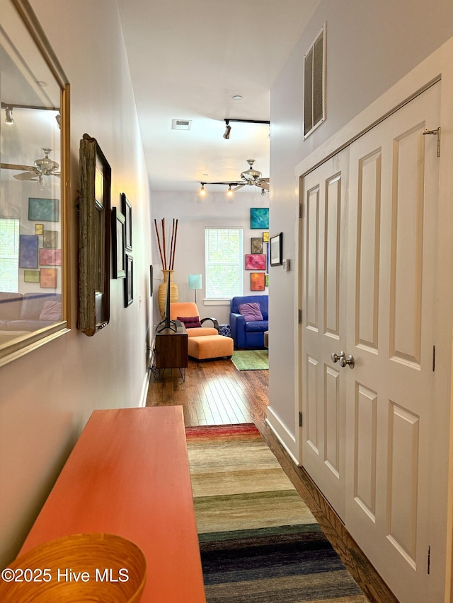 hall with rail lighting, hardwood / wood-style floors, and baseboards