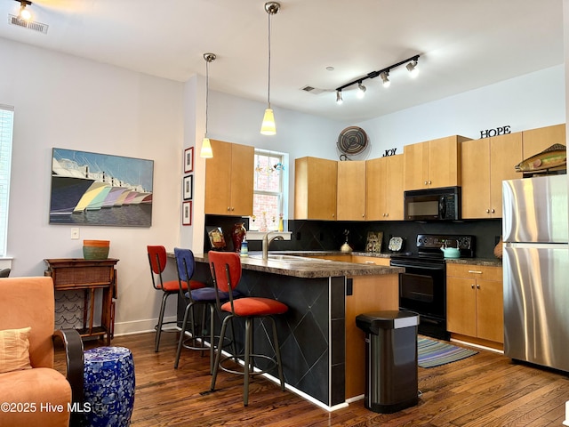 kitchen featuring black appliances, dark countertops, dark wood-style floors, a peninsula, and a breakfast bar