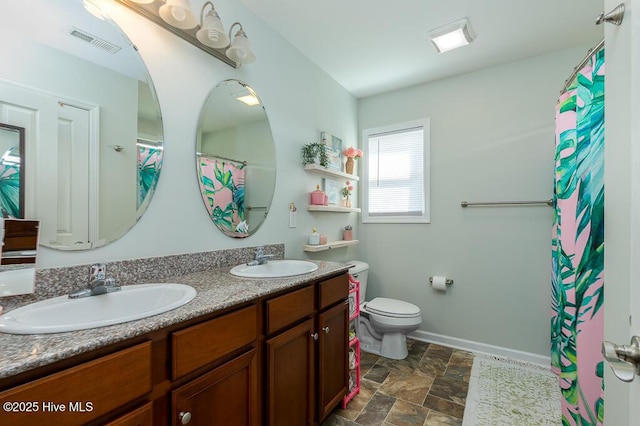 bathroom with toilet, double vanity, stone finish flooring, and baseboards