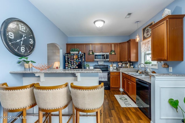 kitchen with black appliances, a sink, a kitchen breakfast bar, dark wood finished floors, and brown cabinetry
