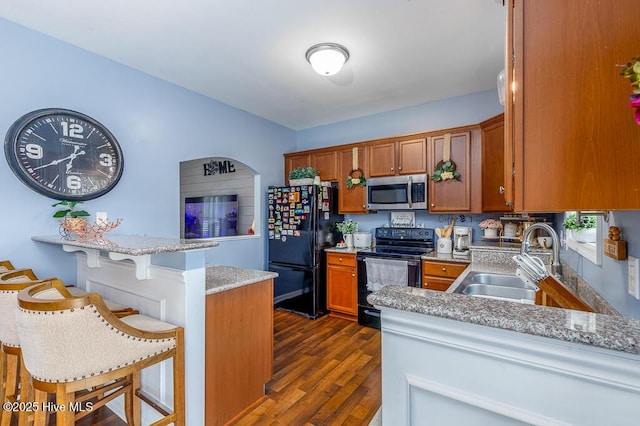 kitchen featuring black appliances, a sink, a peninsula, a kitchen bar, and brown cabinets