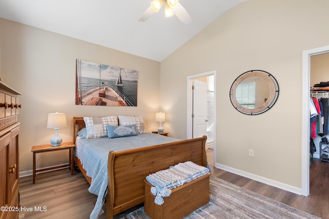 bedroom with a spacious closet, wood finished floors, a closet, baseboards, and high vaulted ceiling