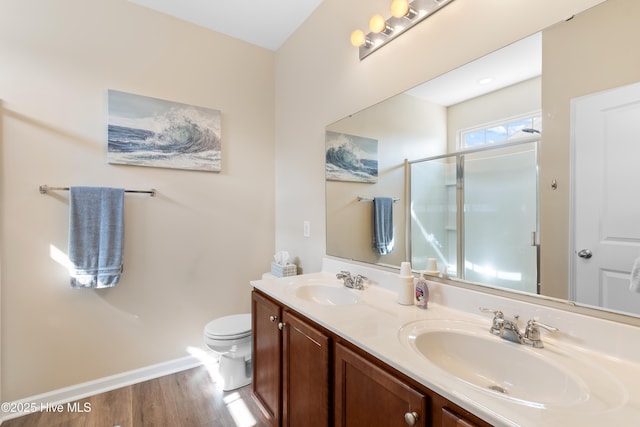bathroom featuring a shower stall, baseboards, toilet, double vanity, and wood finished floors