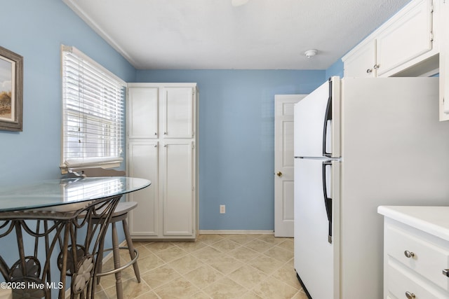 kitchen featuring freestanding refrigerator, baseboards, white cabinets, and light tile patterned flooring