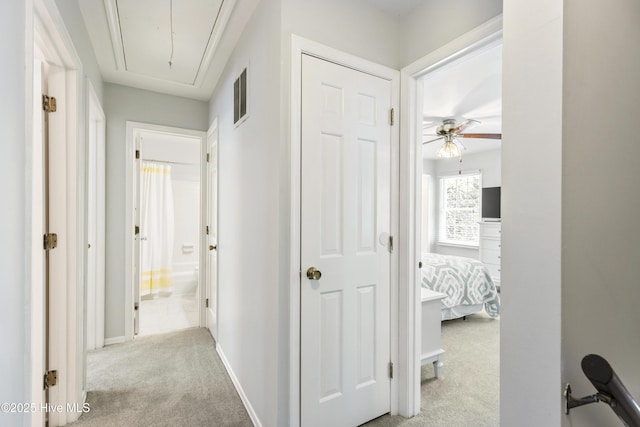 hallway with light carpet, attic access, baseboards, and visible vents