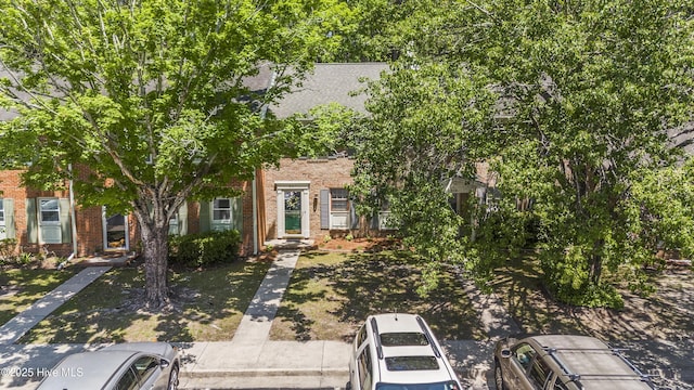 view of property hidden behind natural elements featuring brick siding and uncovered parking