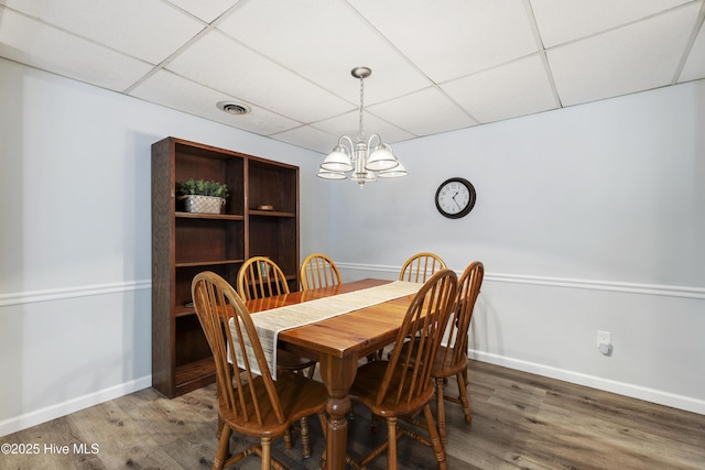 dining area featuring a paneled ceiling, a chandelier, baseboards, and wood finished floors