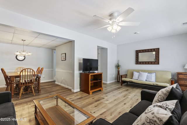 living room with a drop ceiling, baseboards, visible vents, ceiling fan with notable chandelier, and light wood-style floors